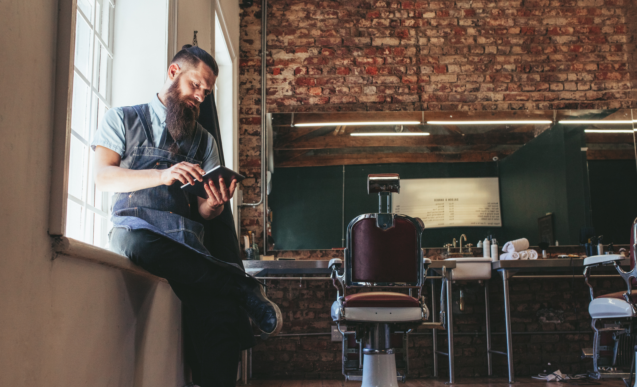 Salon owner using tablet to manage bookings and marketing campaigns with salon software in a modern barbershop